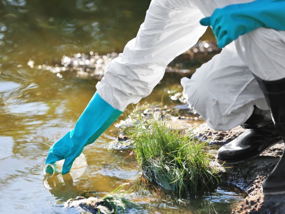 person wearing gloves collects a sample of water