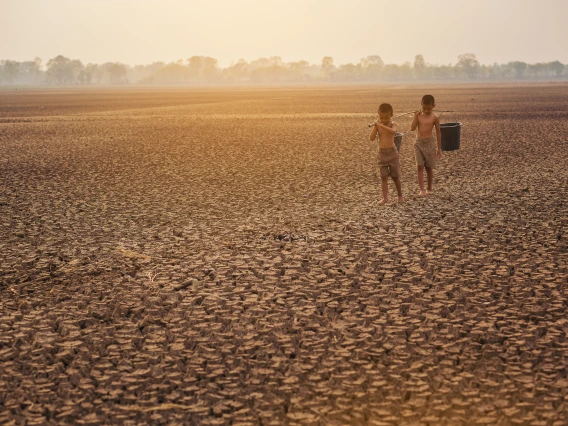 two children walking through dirt with a bucket