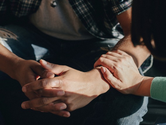 man's hands folded while woman's hand touches in comfort