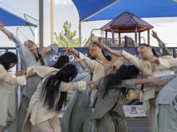 Several dancers in neutral-colored flowing clothes lift their arms and bend their bodies during a dance. 