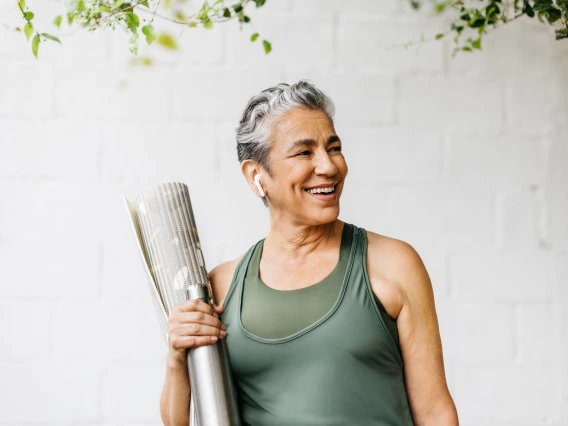 woman in green tank holding water bottle and yoga mat