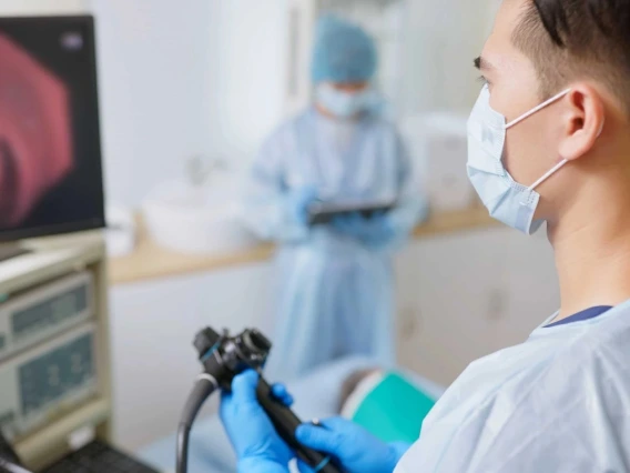 A doctor wearing surgical gear looks at a computer screen as he conducts a colonoscopy on a patient.