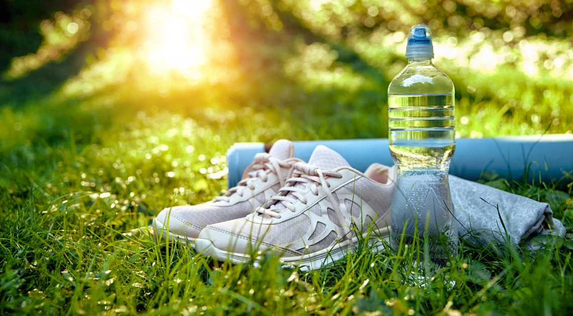 Sneakers, water bottle and workout towel on grassy field.