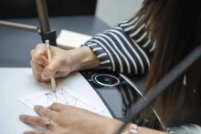 Close-up photo of a hand gripping a pencil, doodling on paper.