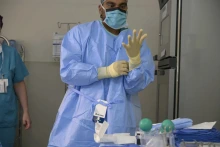 Health care worker in mask and surgical gown putting on a glove