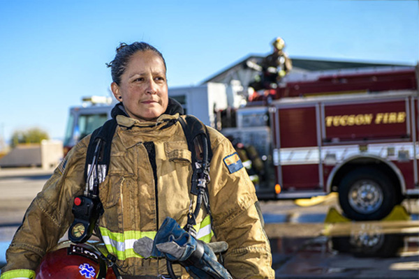 Female firefighter with firetruck in background spraying hose