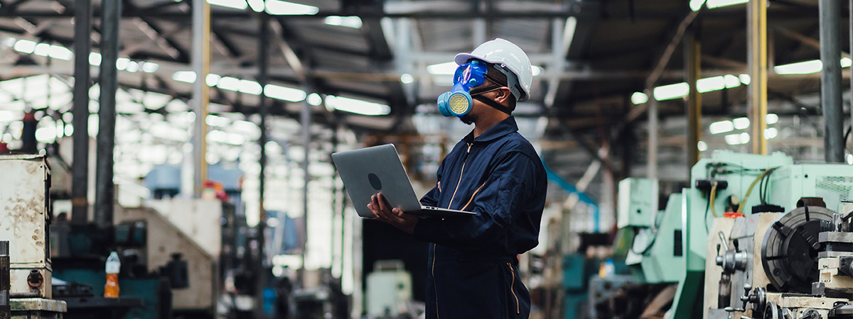 Man with protective mask and computer laptops in factory